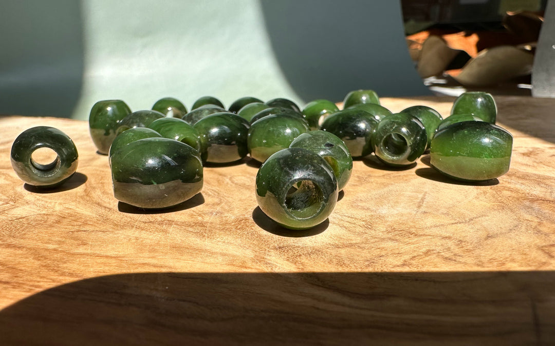 Close up of green jade barrel beads with holes on a wooden table