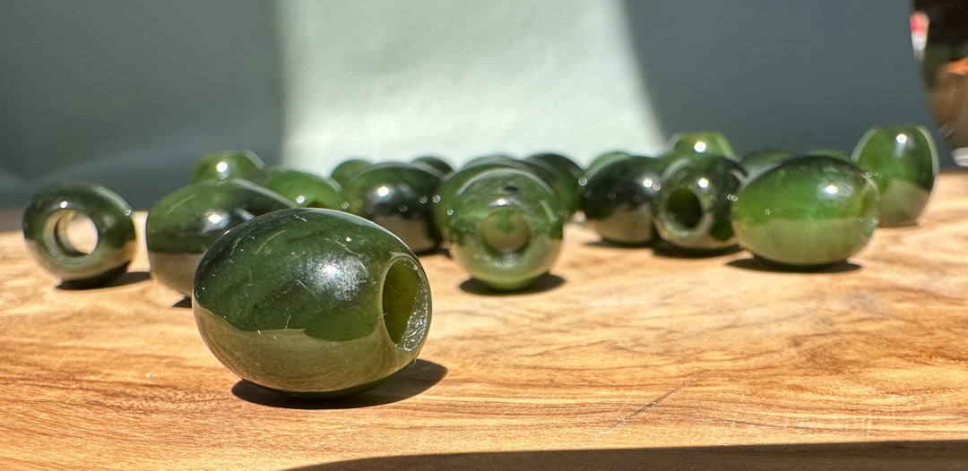 Green jade barrel beads 15x12mm with holes on a wooden table seen from a low angle