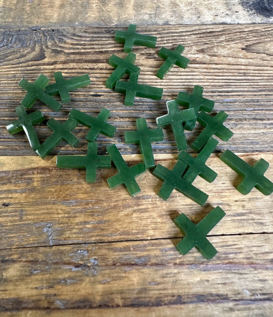 Loose drilled green jade cross charms, 20mm, scattered on a rustic wooden surface