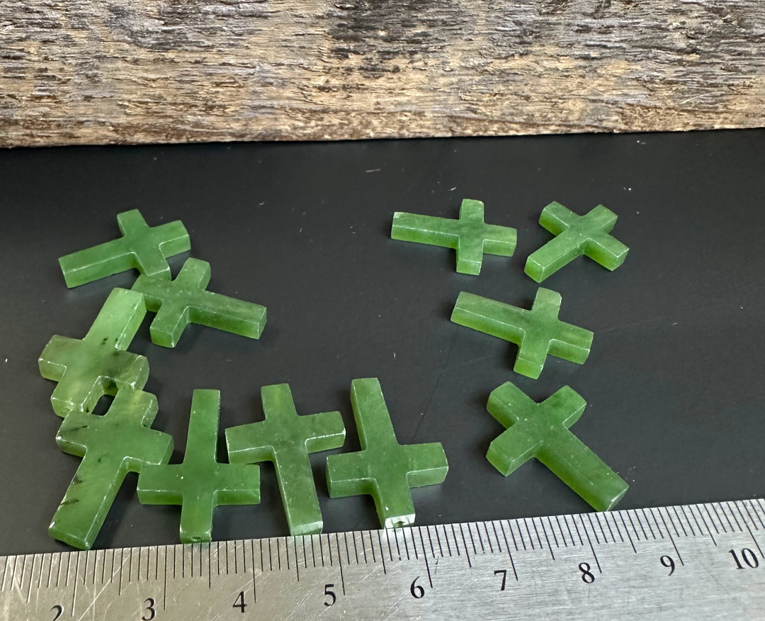 Multiple green jade cross charms scattered on a black surface with a ruler for scale