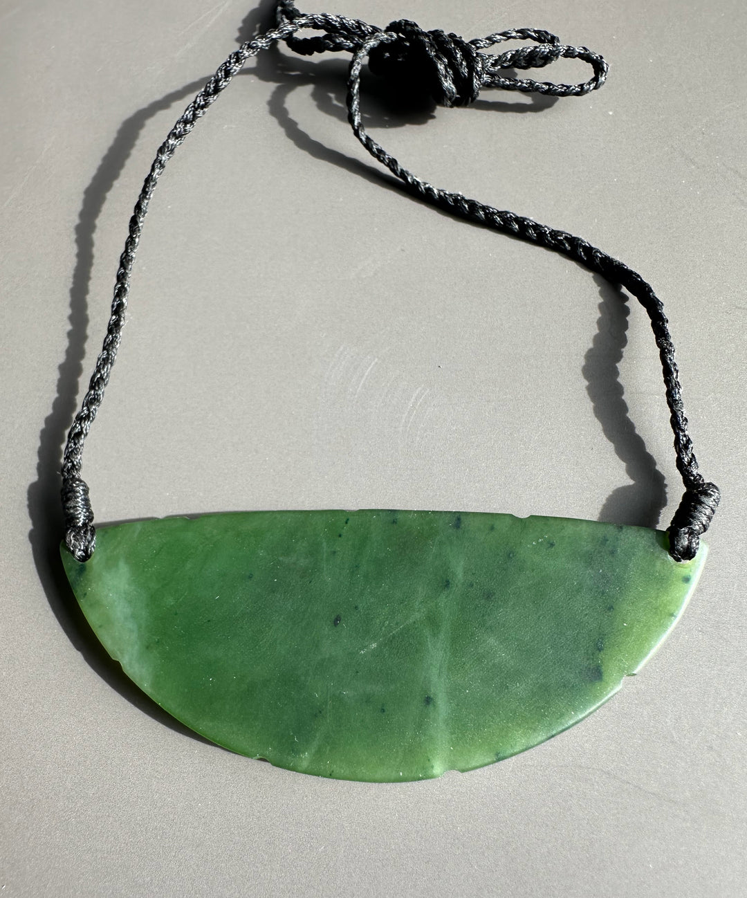 Green jade crescent pendant on a braided black cord.
