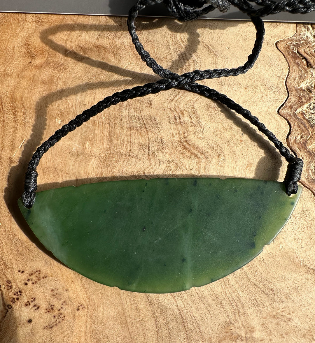 Close-up of green jade pendant on a black braided cord resting on wood.