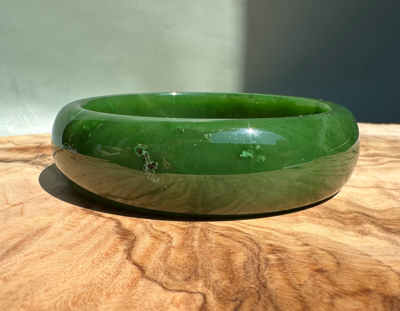 AA Canadian Jade Bangle two tone green and beige outer band on a wooden surface in bright light