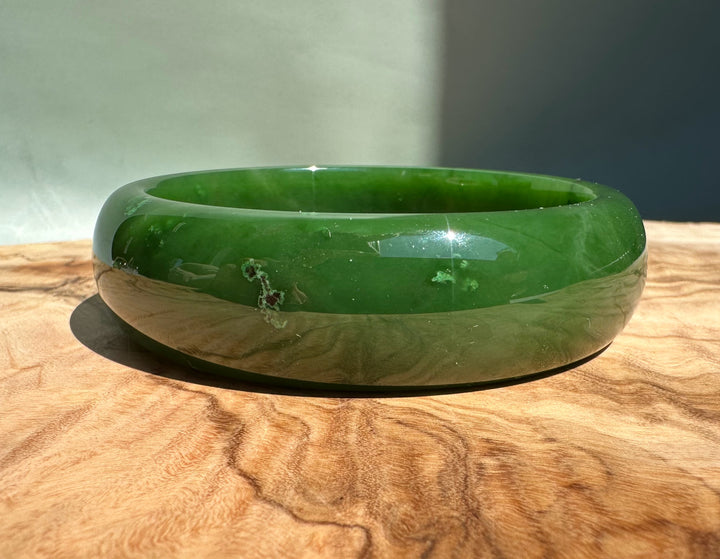AA Canadian Jade Bangle two tone green and beige outer band on a wooden surface in bright light