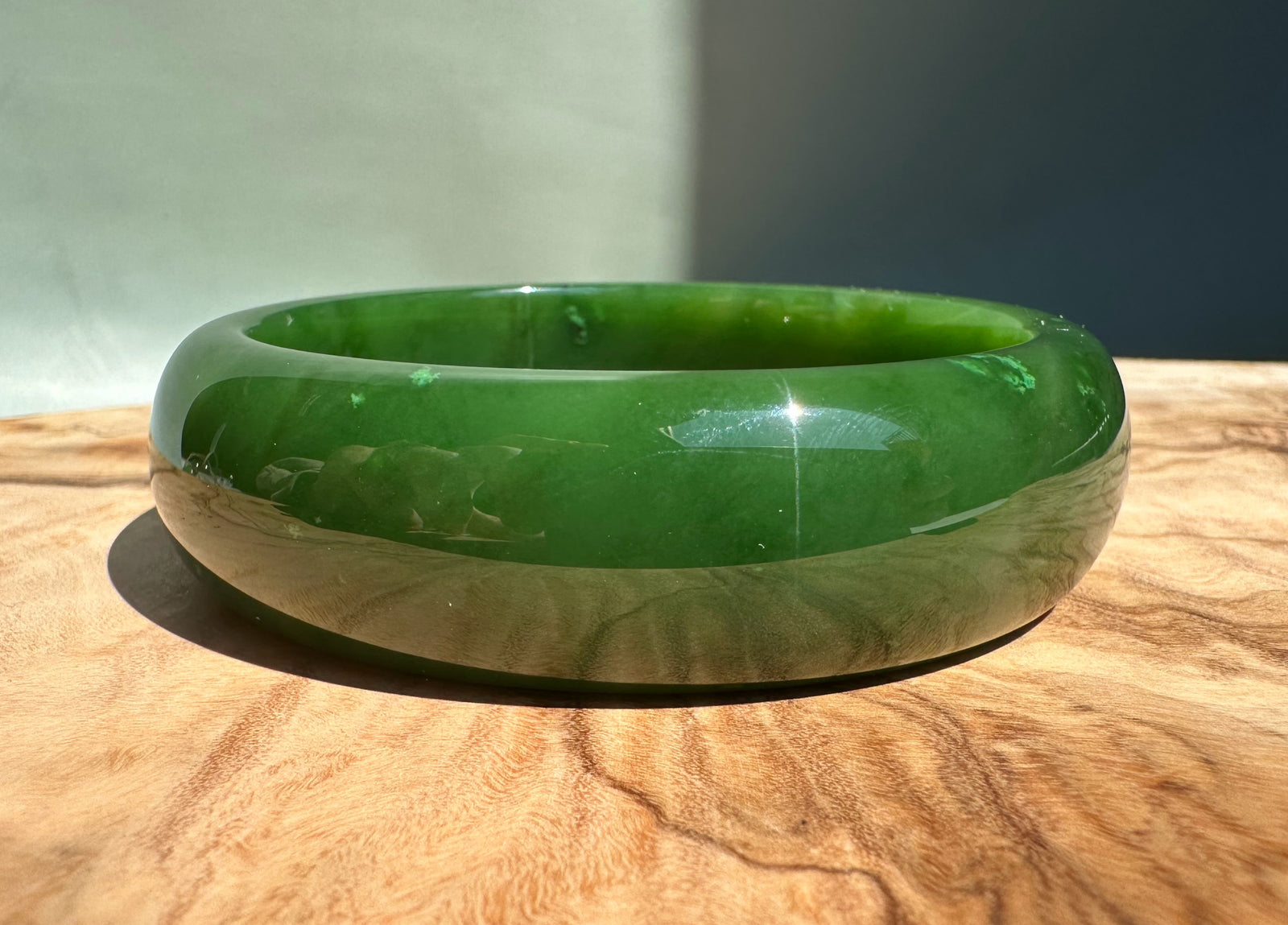 AA Canadian Jade Bangle in emerald green with a smooth glossy finish on a wooden surface