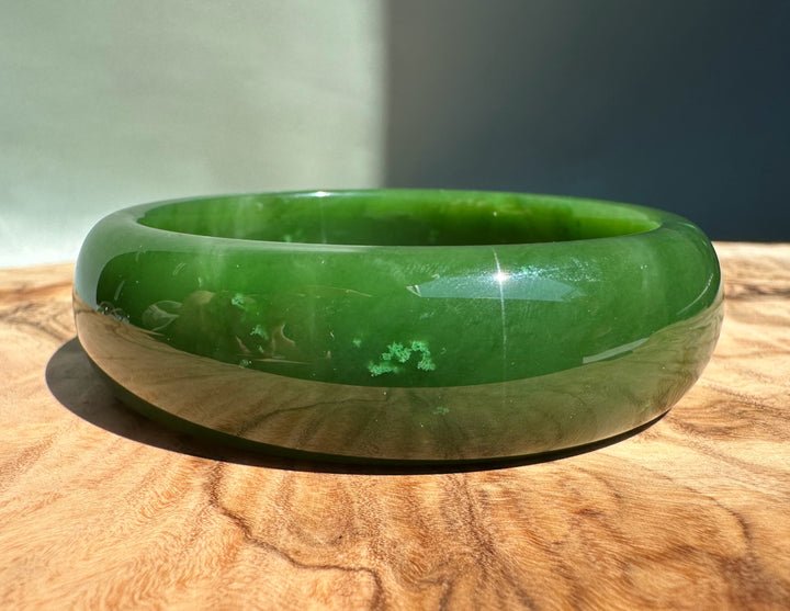 AA Canadian Jade Bangle 60x19mm in vivid green resting on a wooden surface.