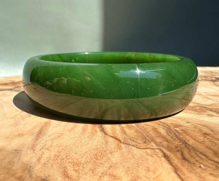 AA Canadian Jade Bangle 60x19mm on a wooden surface, glossy emerald green.