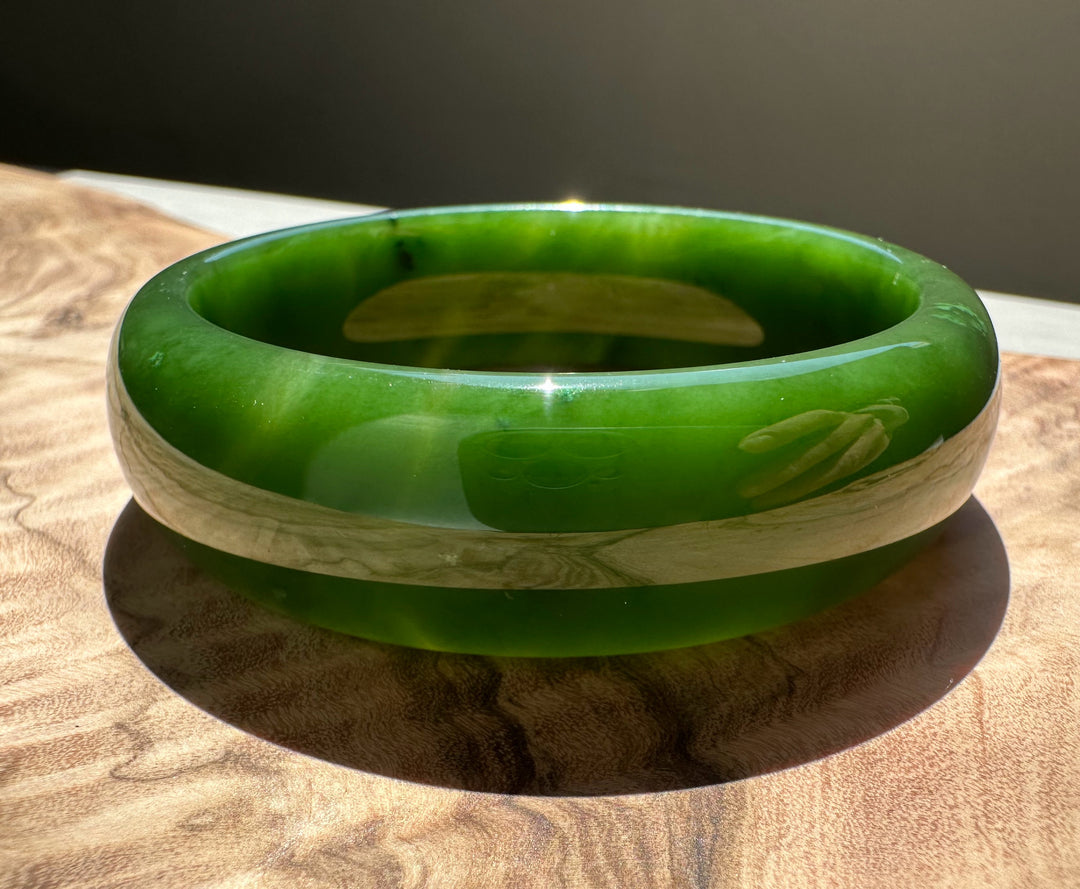 AA Canadian Jade Bangle 60x19mm in bright green jade on a wood surface
