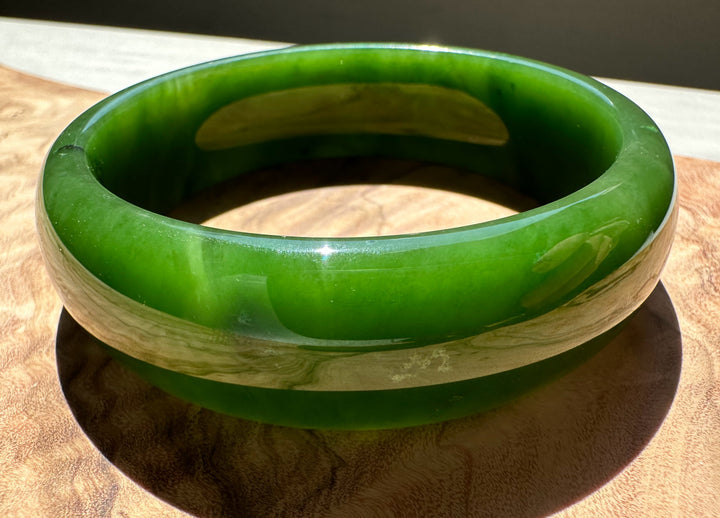 AA Canadian Jade Bangle 60x19mm in emerald green with lighter inner edge on a wooden surface