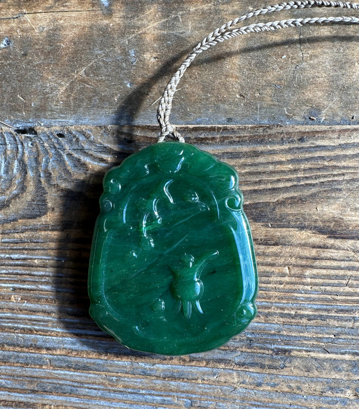 Front view of a green jade Guanyin pendant with carved details on wood