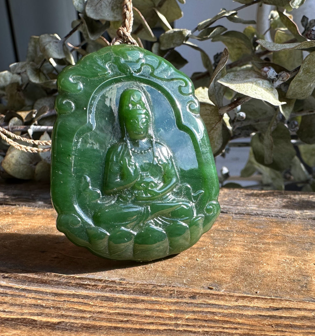 Green jade Guanyin pendant with seated figure carved in relief and a cord.