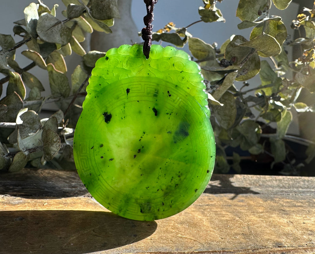Neon green jade pendant oval shape with carved border and looped brown cord