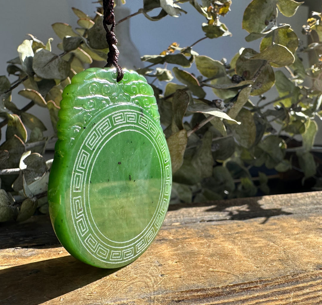 Bright green circular jade pendant with a geometric border on a brown cord