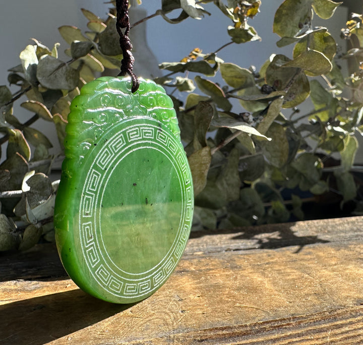 Bright green circular jade pendant with a geometric border on a brown cord