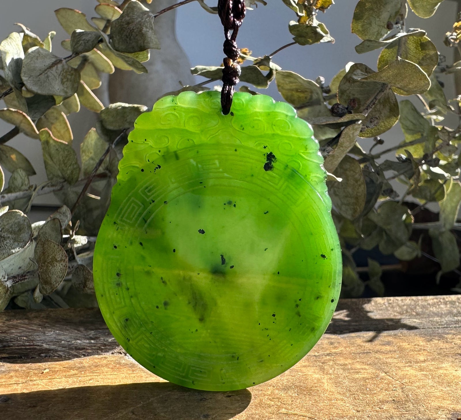 Close up of the bright green jade pendant showing a geometric border and cord