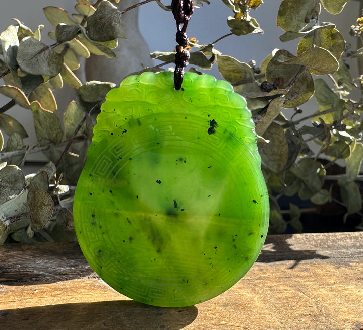 Close up of the bright green jade pendant showing a geometric border and cord