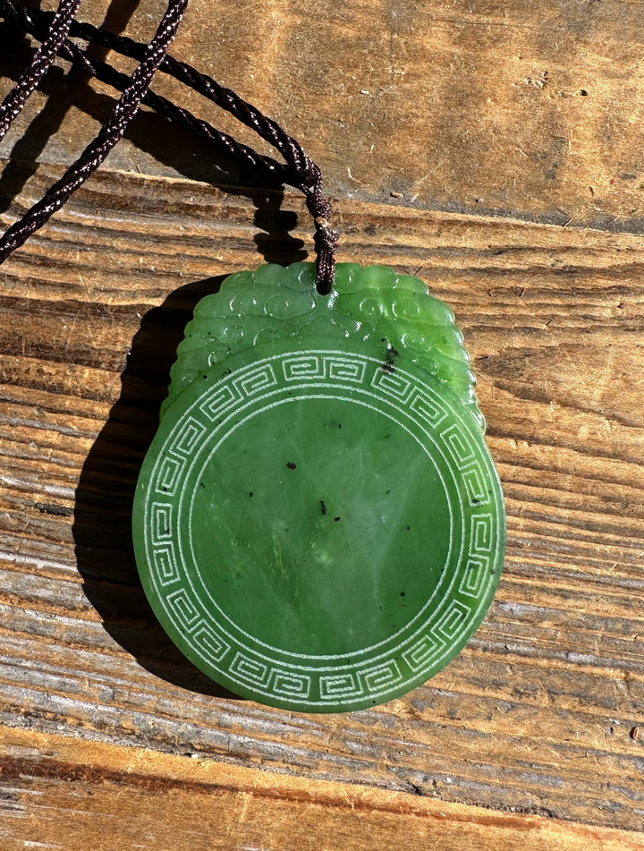 Green jade pendant with circular pattern and square meander border on brown cord