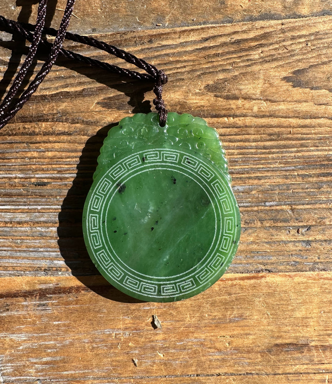 Jade pendant with circular border and cloud-like top detail on a brown cord