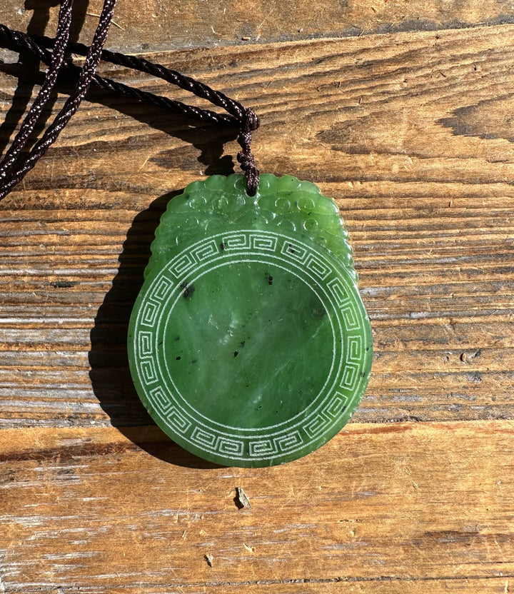 Jade pendant with circular border and cloud-like top detail on a brown cord
