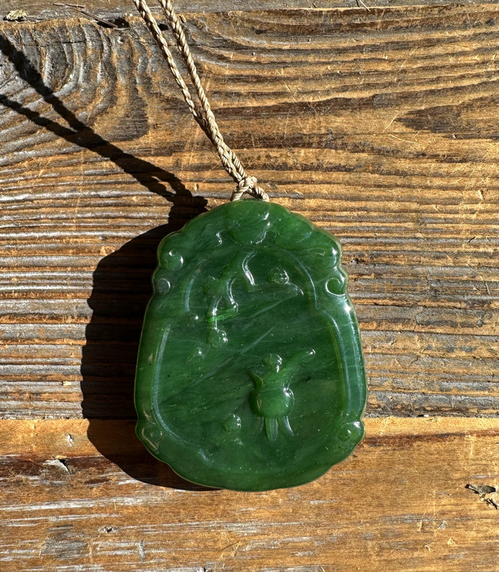 Green jade Guanyin pendant on a braided cord against a rustic wooden surface