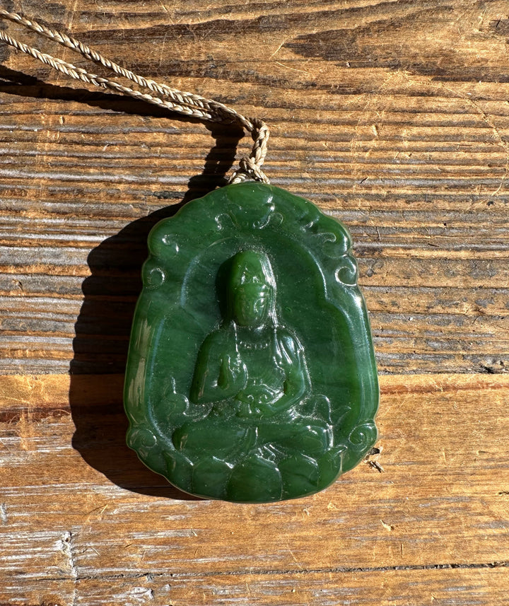 Close up of green jade Guanyin pendant showing the carved seated figure against a wooden surface.