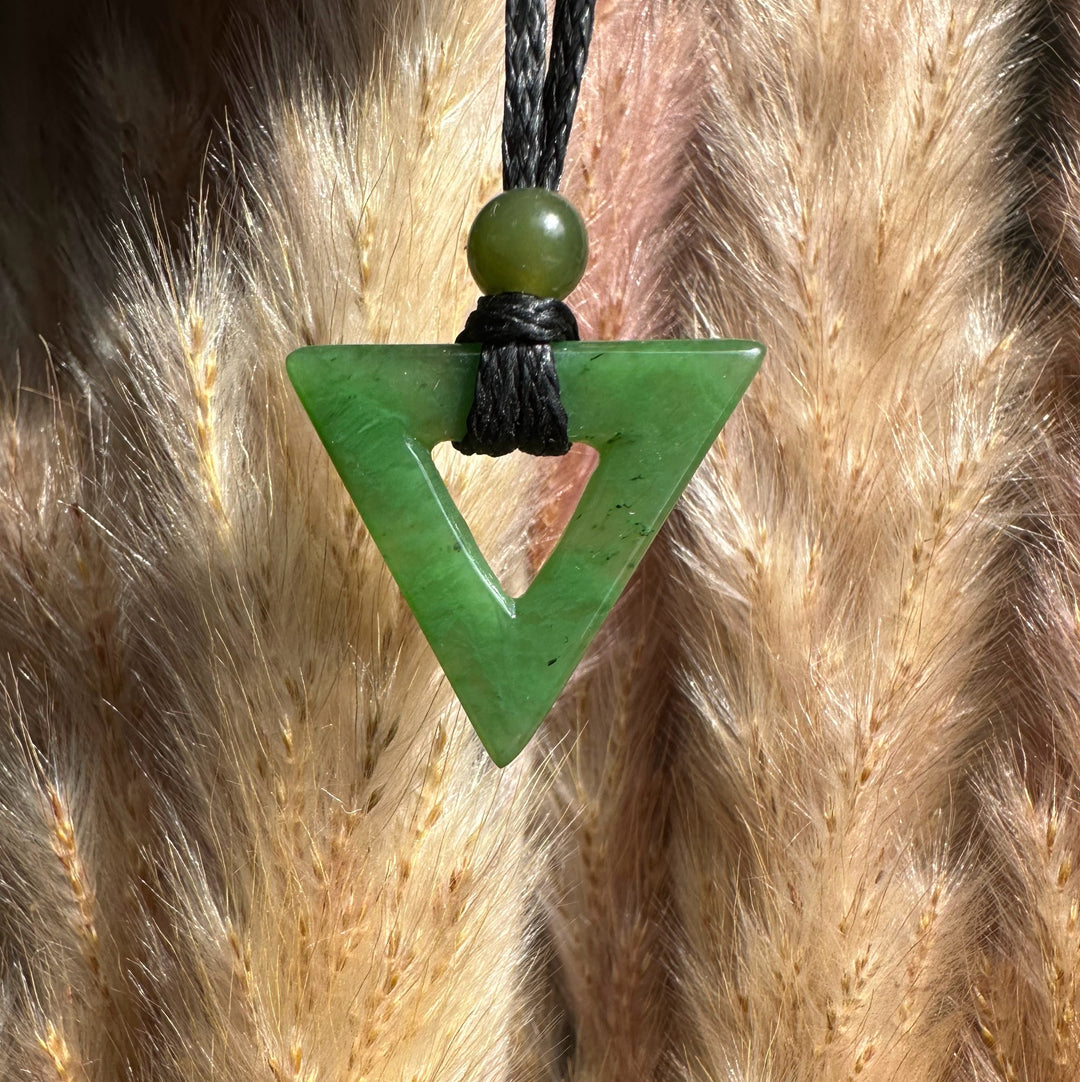 Green jade triangle pendant with hollow center on a black cord and bead
