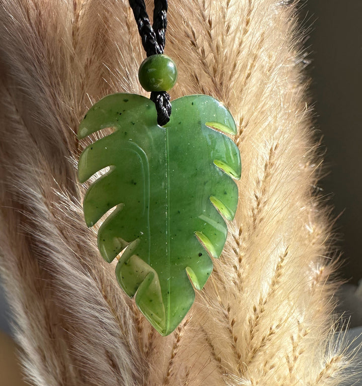 Jade monstera leaf pendant on a black braided cord with a small bead above.