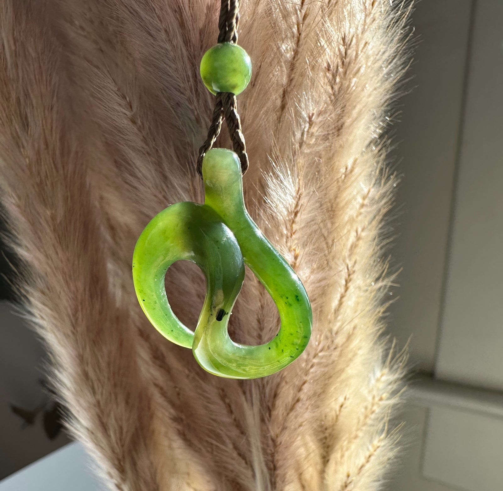 Bright green jade pendant with an abstract looping shape on a brown braided cord.
