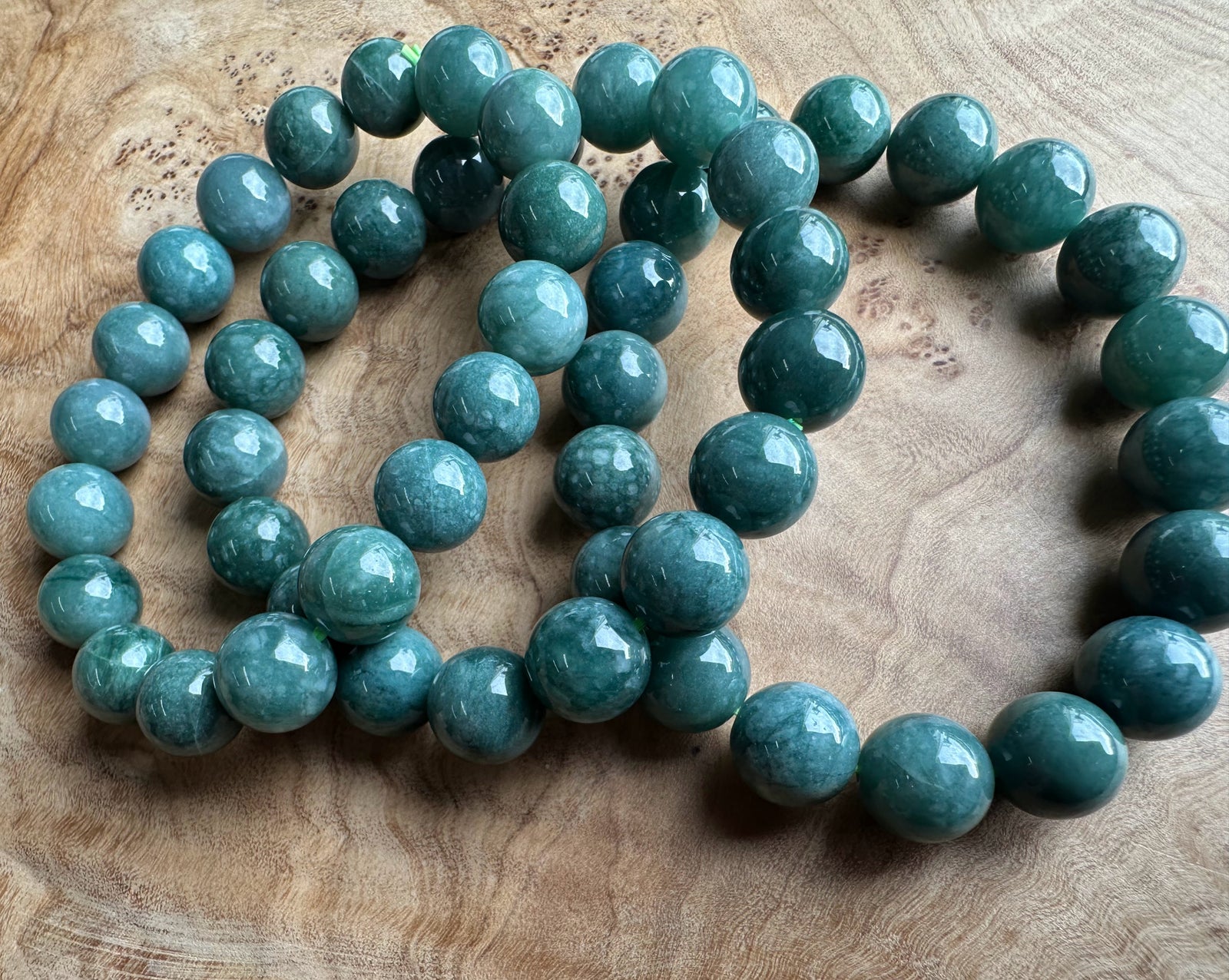 Teal-green jadeite beads 10mm laid on a wooden surface, glossy round stones