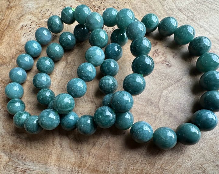 Teal-green jadeite beads 10mm laid on a wooden surface, glossy round stones