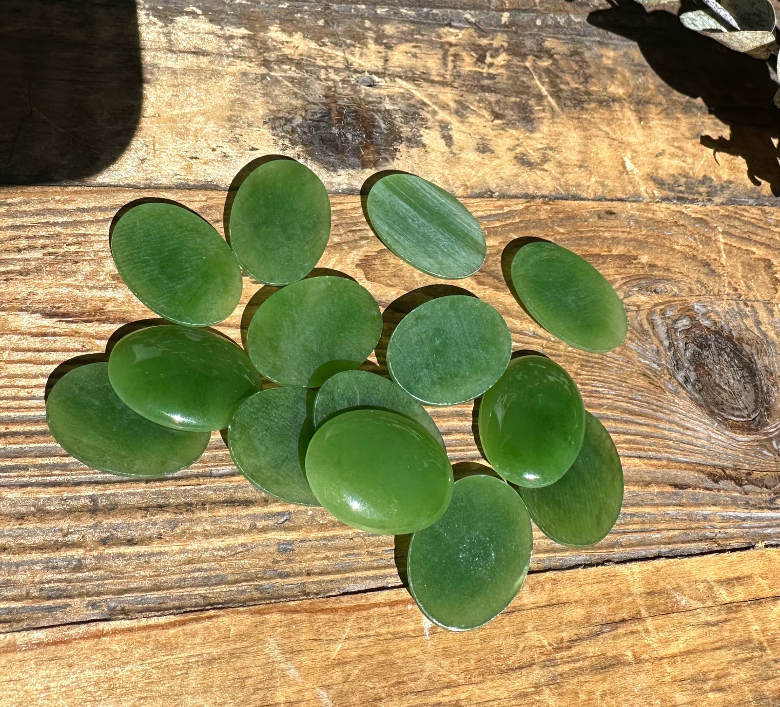 Group of green nephrite jade oval cabochons 18 by 25 mm on a wooden surface.
