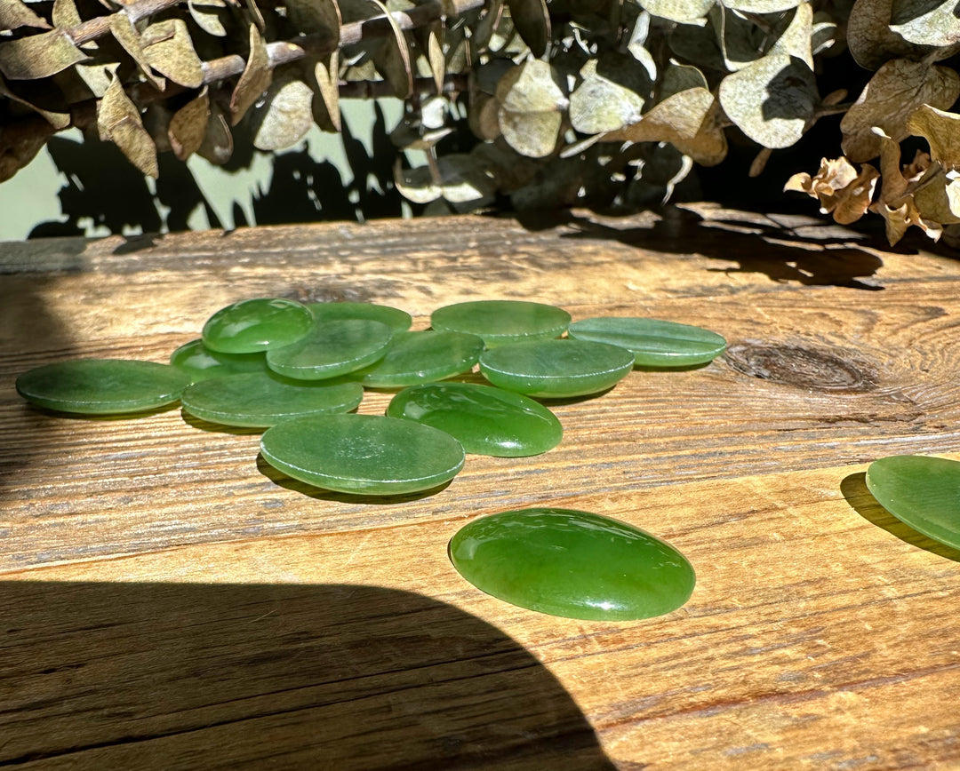 Cluster of oval nephrite jade cabochons 18x25mm scattered on a wooden table with dried greenery in the background