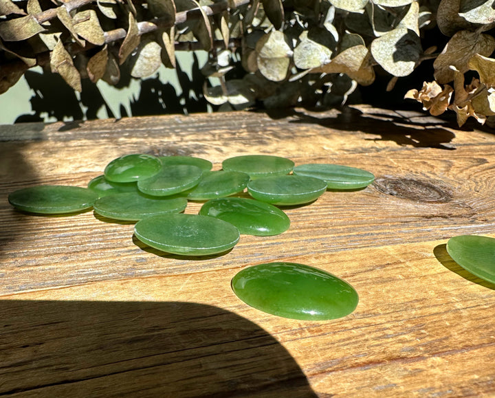 Cluster of oval nephrite jade cabochons 18x25mm scattered on a wooden table with dried greenery in the background