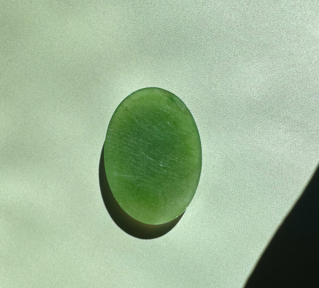 Single Canadian nephrite jade oval cabochon 18x25mm on a pale green background.