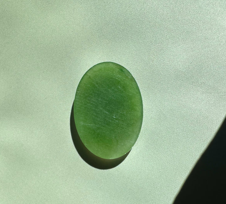 Single Canadian nephrite jade oval cabochon 18x25mm on a pale green background.