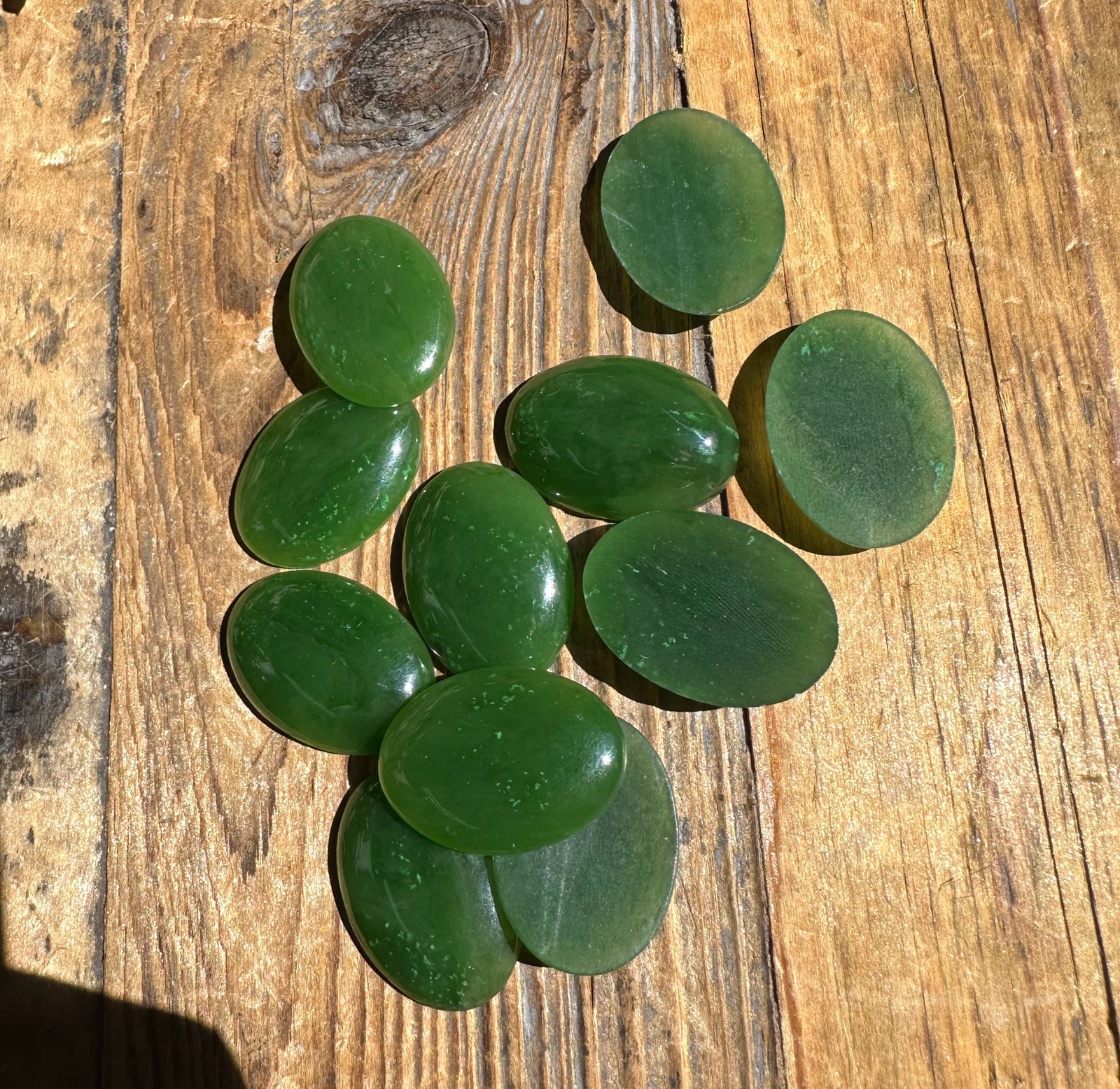Medium green jade oval cabochons 18x25mm scattered on a sunlit wooden surface