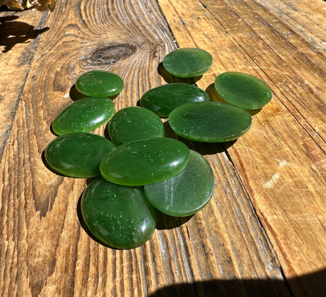Oval green jade cabochons scattered on a sunlit wooden surface
