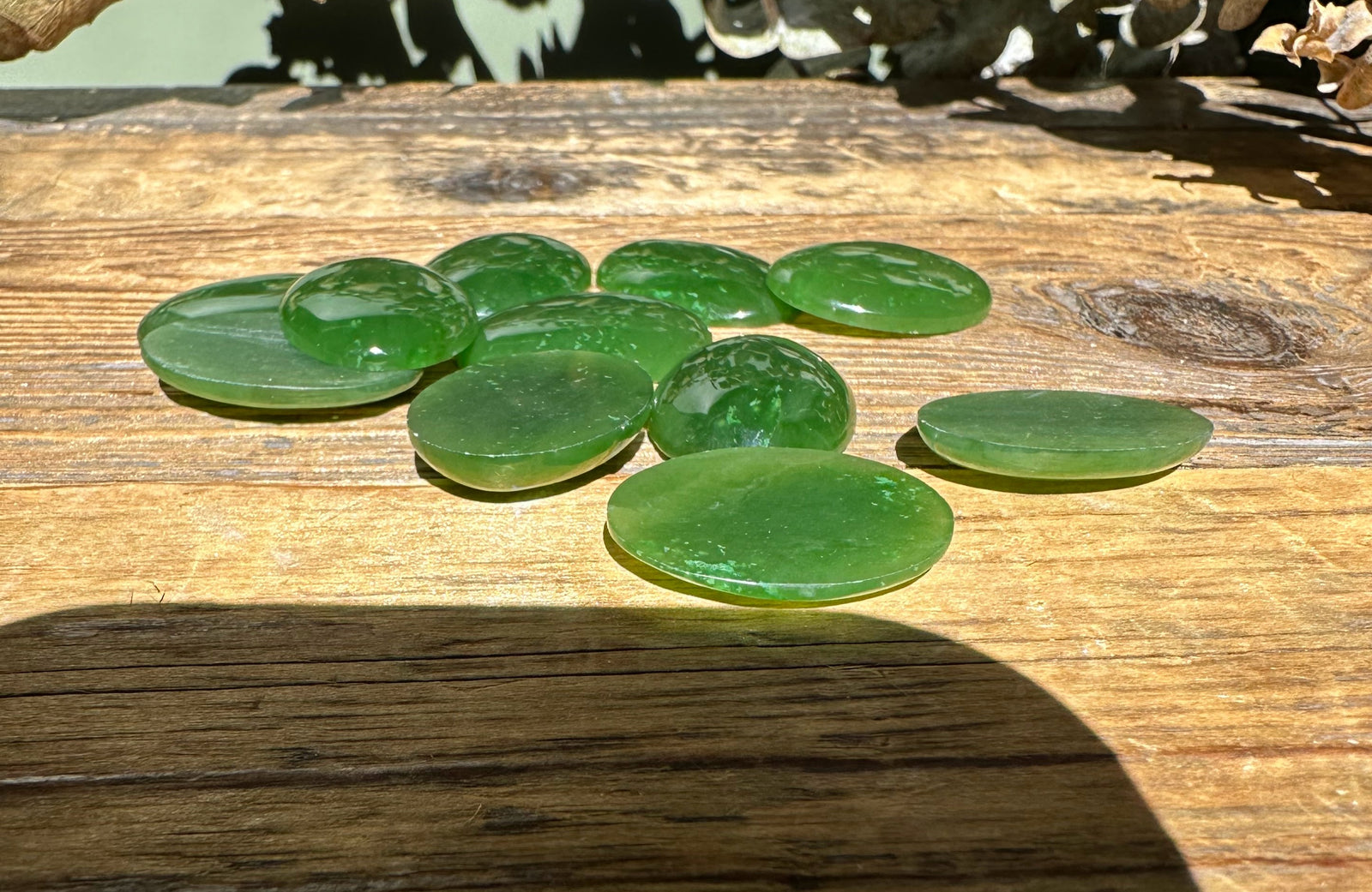 Group of oval 18x25mm green jade cabochons displayed on a rustic wooden surface