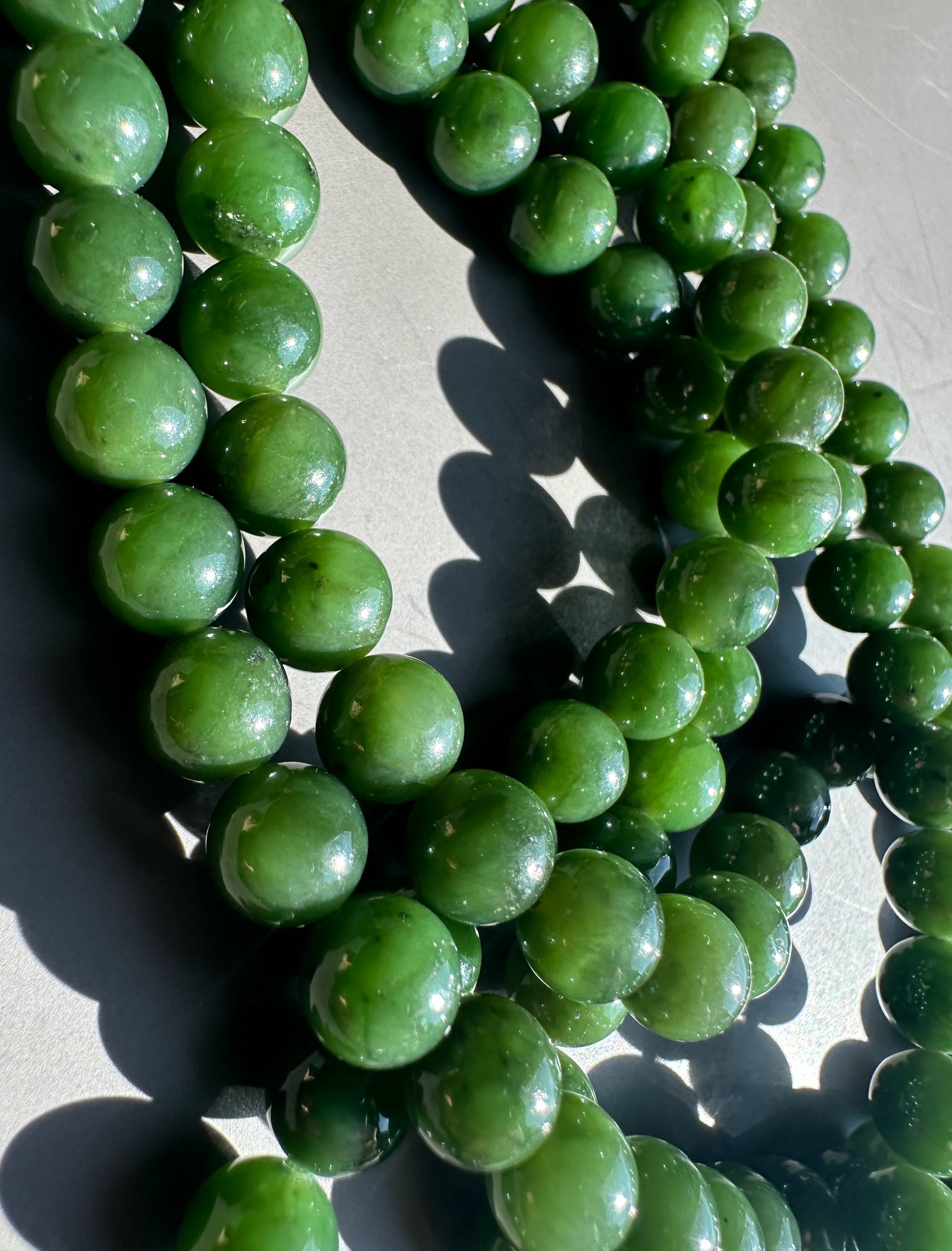 Closeup of glossy dark green 8mm Canadian beads arranged in loops on a light surface