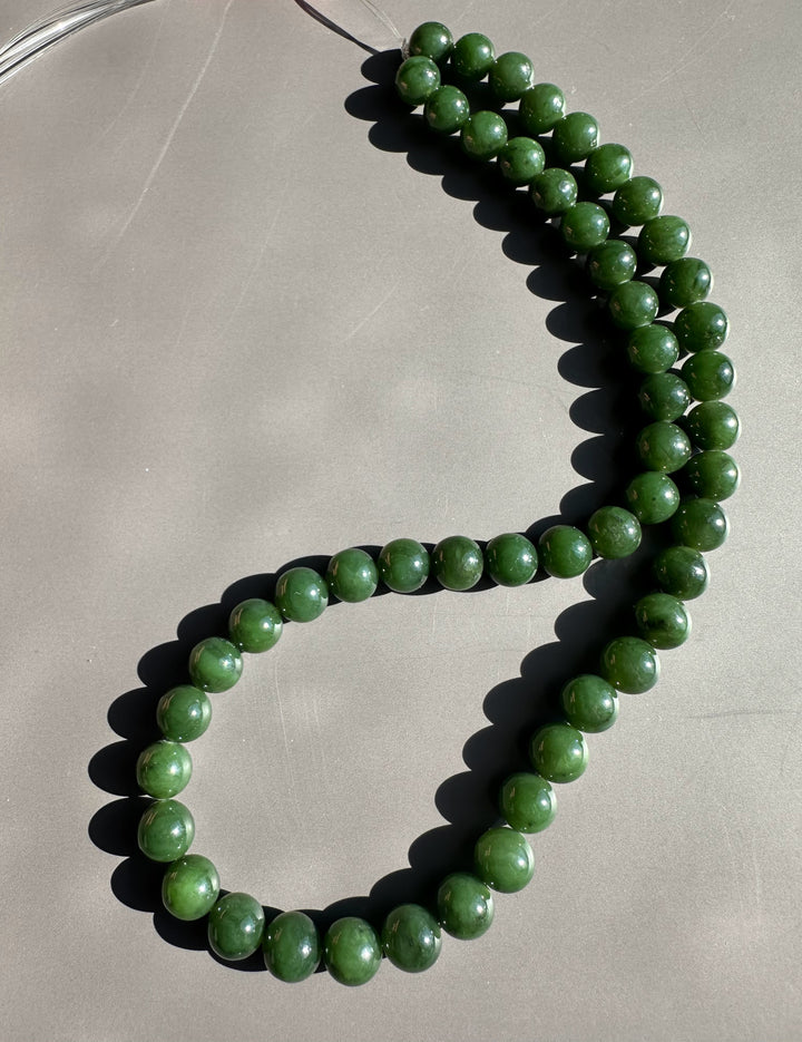 8mm dark green Canadian unstrung bead strand curved on a gray table