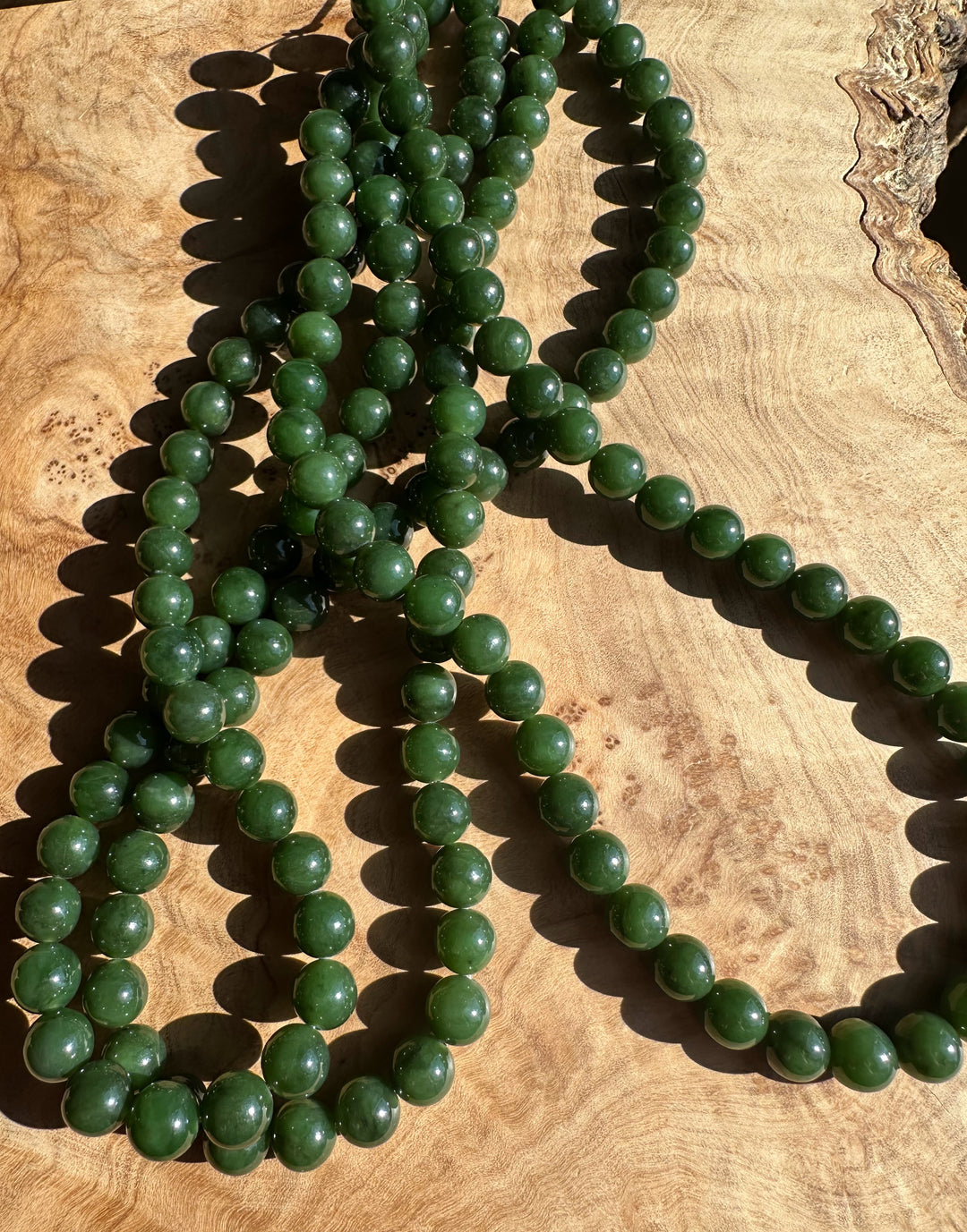 Dark green 8mm Canadian unstrung beads arranged in several strands on a wooden surface.