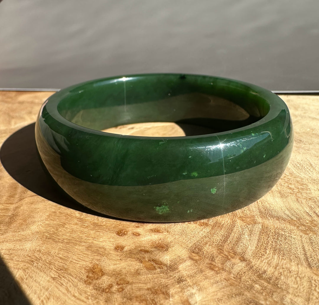 Canadian Jade Bangle in deep green with a glossy polished finish on a wooden surface