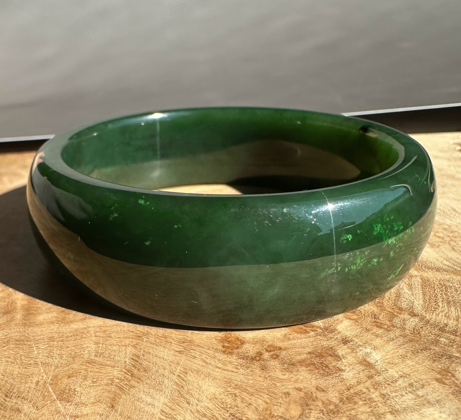 Green jade bangle 60.5 x 20mm with a glossy finish resting on a wooden surface.