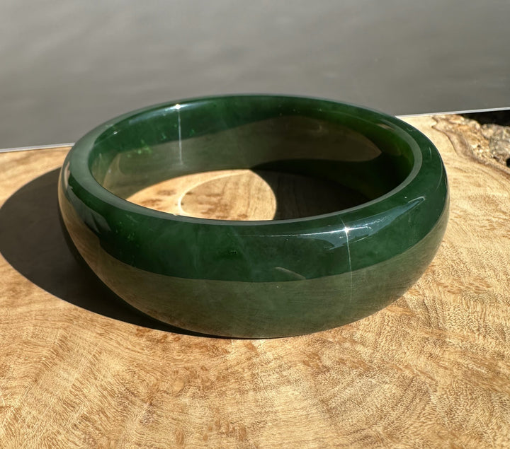 Canadian Jade Bangle in rich green with a gleaming finish shown on a wooden surface