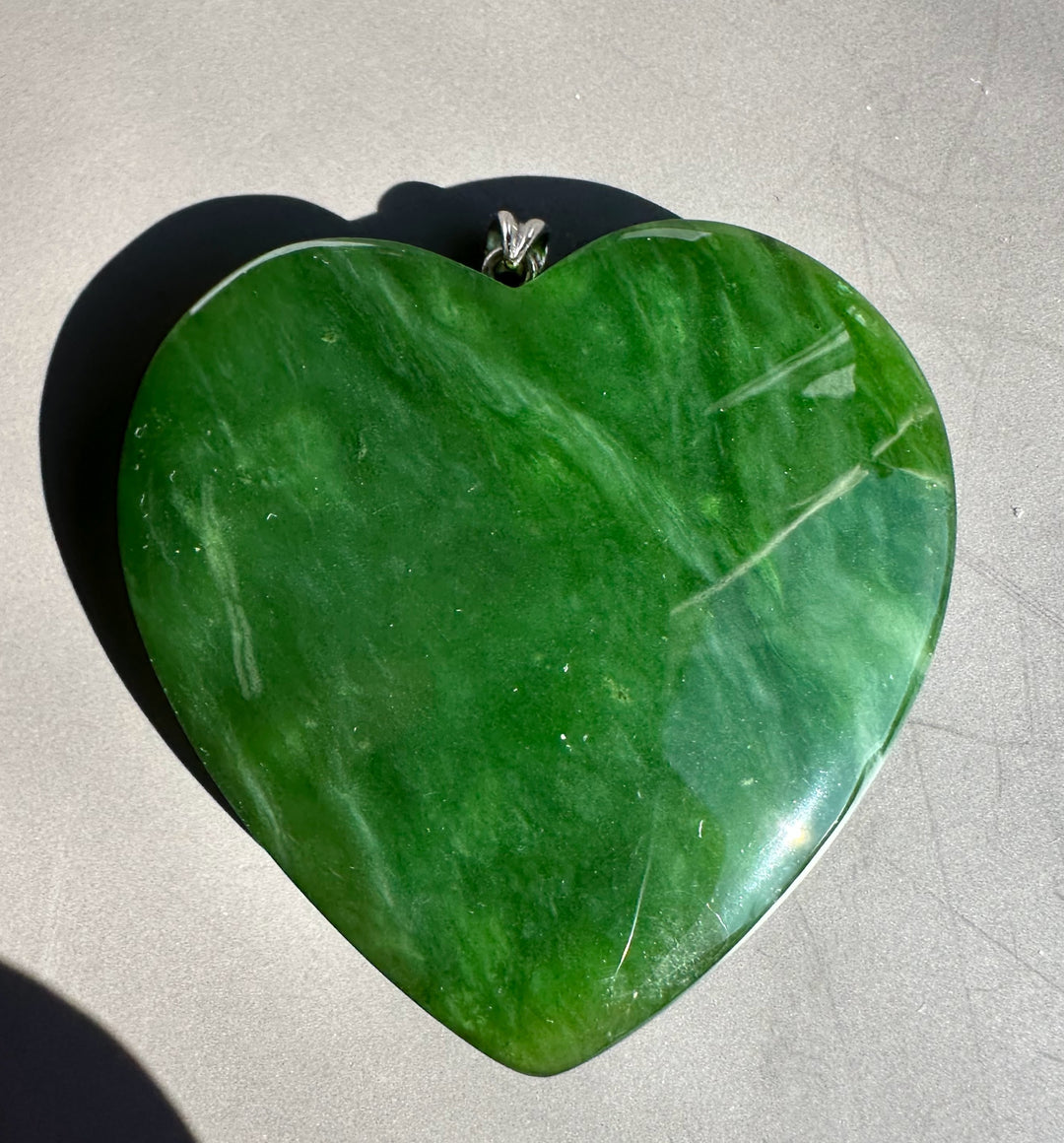 Top down view of a large green polar jade heart pendant with a silver bail on a gray background