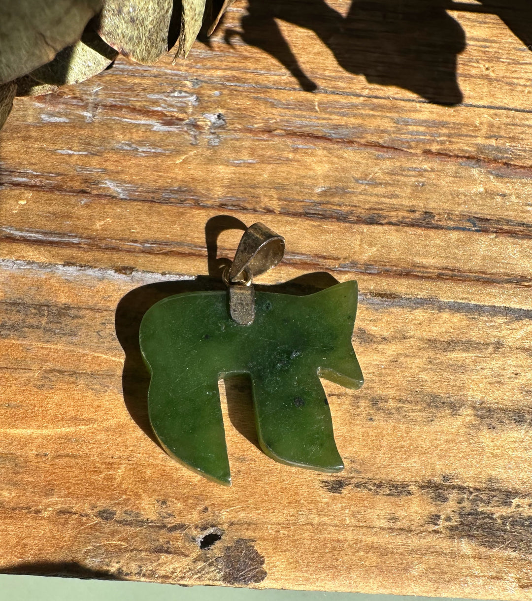 Dark green jade Chai pendant with a metal bail on a wooden surface