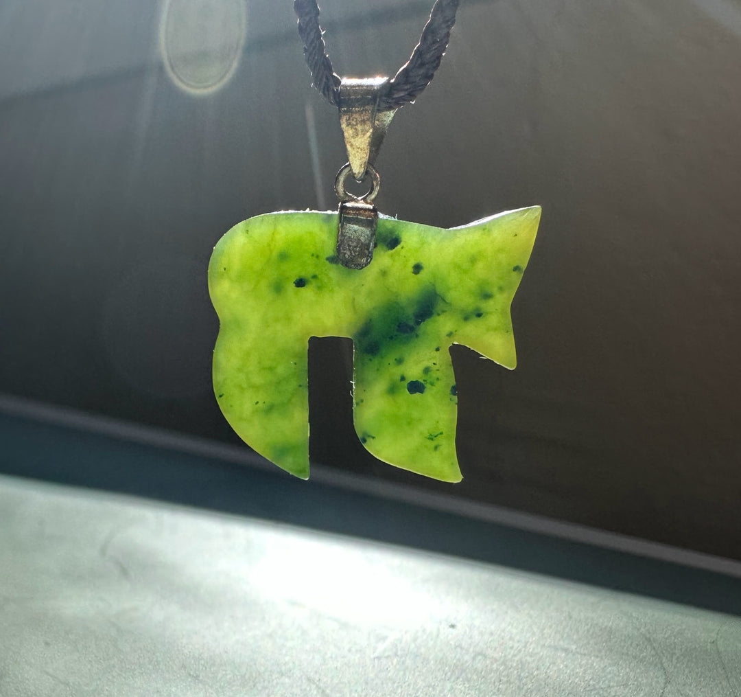 Lime green jade Chai pendant on a black braided cord against a dark background