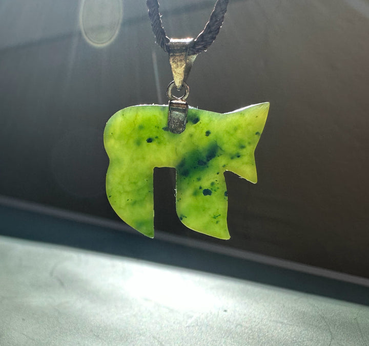 Lime green jade Chai pendant on a black braided cord against a dark background