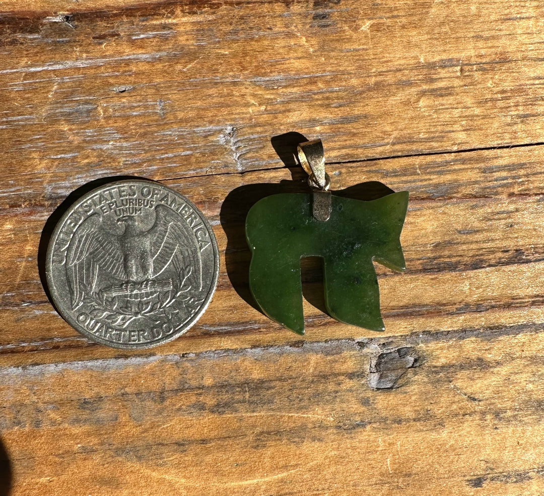 Green carved jade pendant in a teardrop shape beside a quarter on a wooden surface