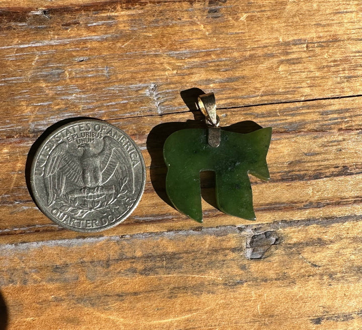 Green carved jade pendant in a teardrop shape beside a quarter on a wooden surface